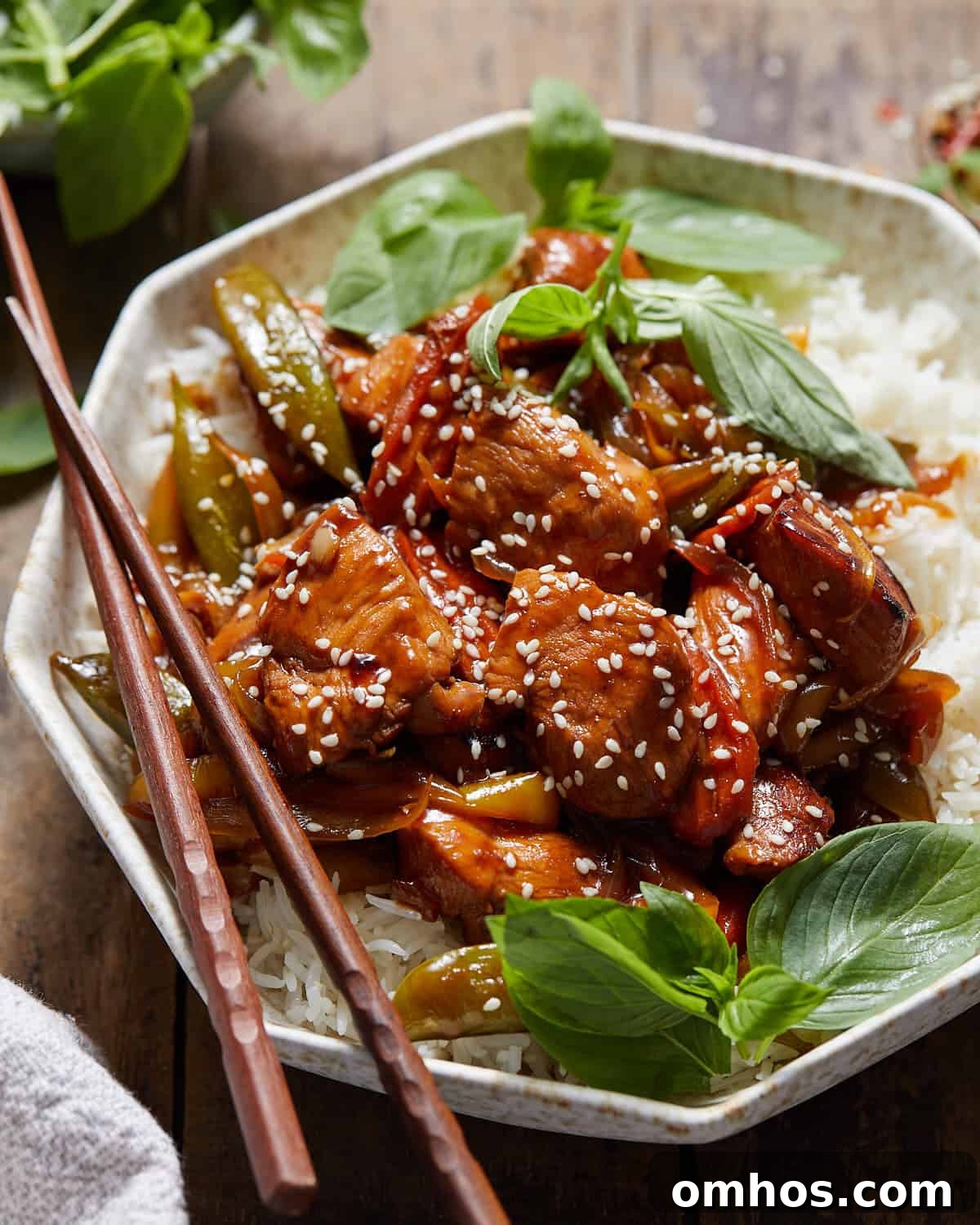 Chicken stir fry over rice in a bowl with chopsticks.