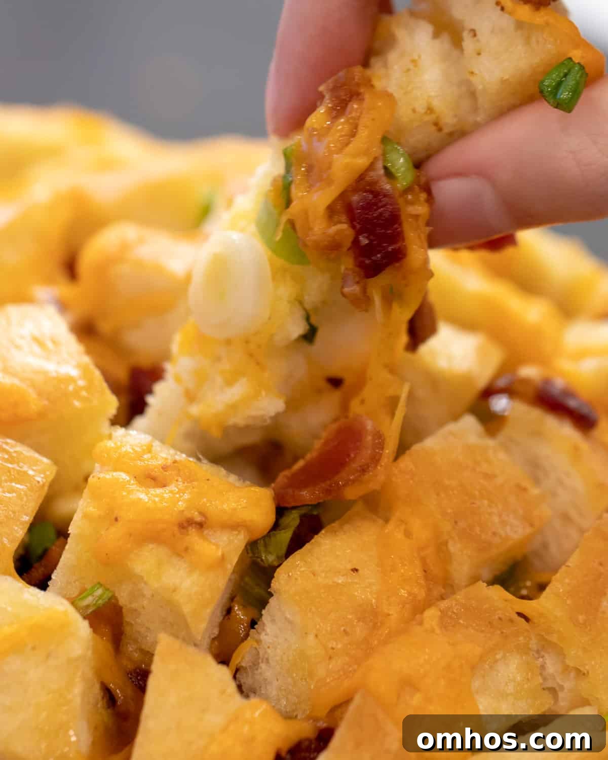A piece of bread being pulled out of the loaf with bacon and cheese stuck all over it.