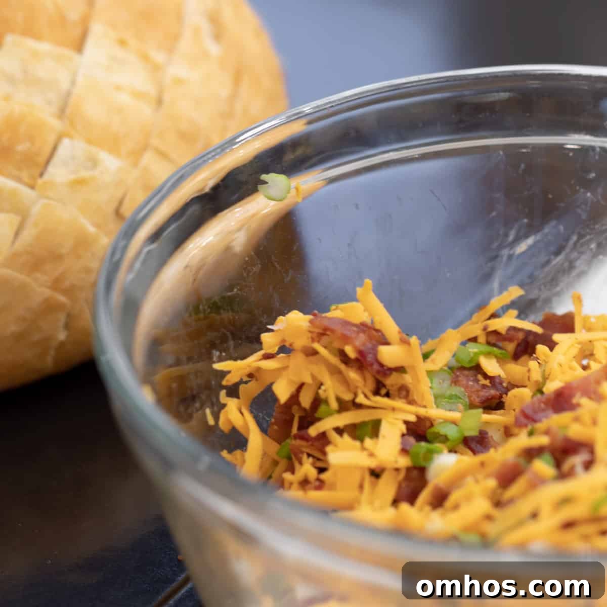 A glass mixing bowl with bacon, grated cheese and sliced green onions.