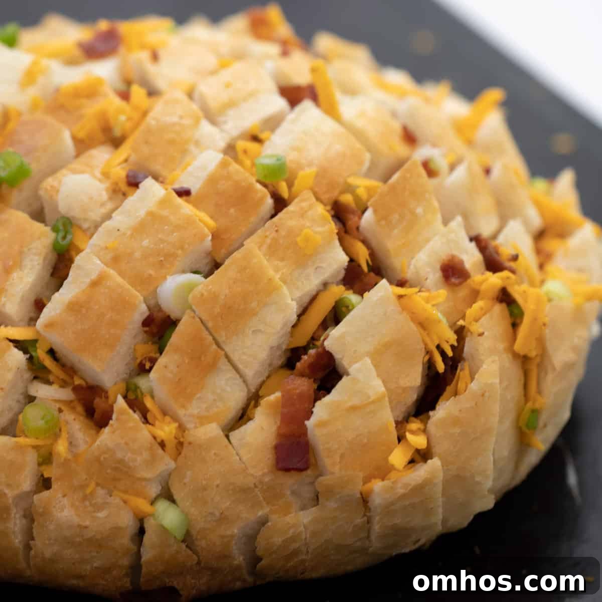 A round loaf of bread with cheese, bacon and onions stuffed through the slits all throughout the bread.