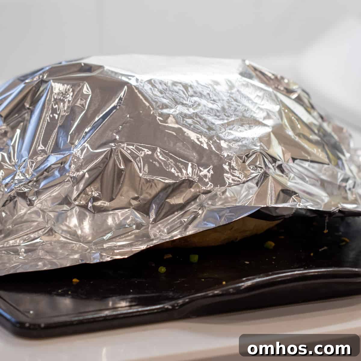 Aluminum foil covering a loaf of bread on a baking stone.