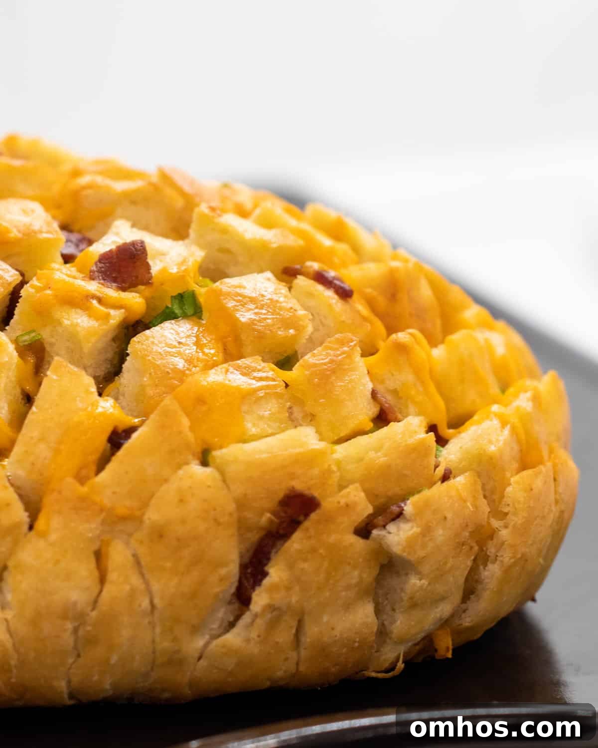 A side photo of a loaf of bread with bacon, cheese and onions baked all in it.