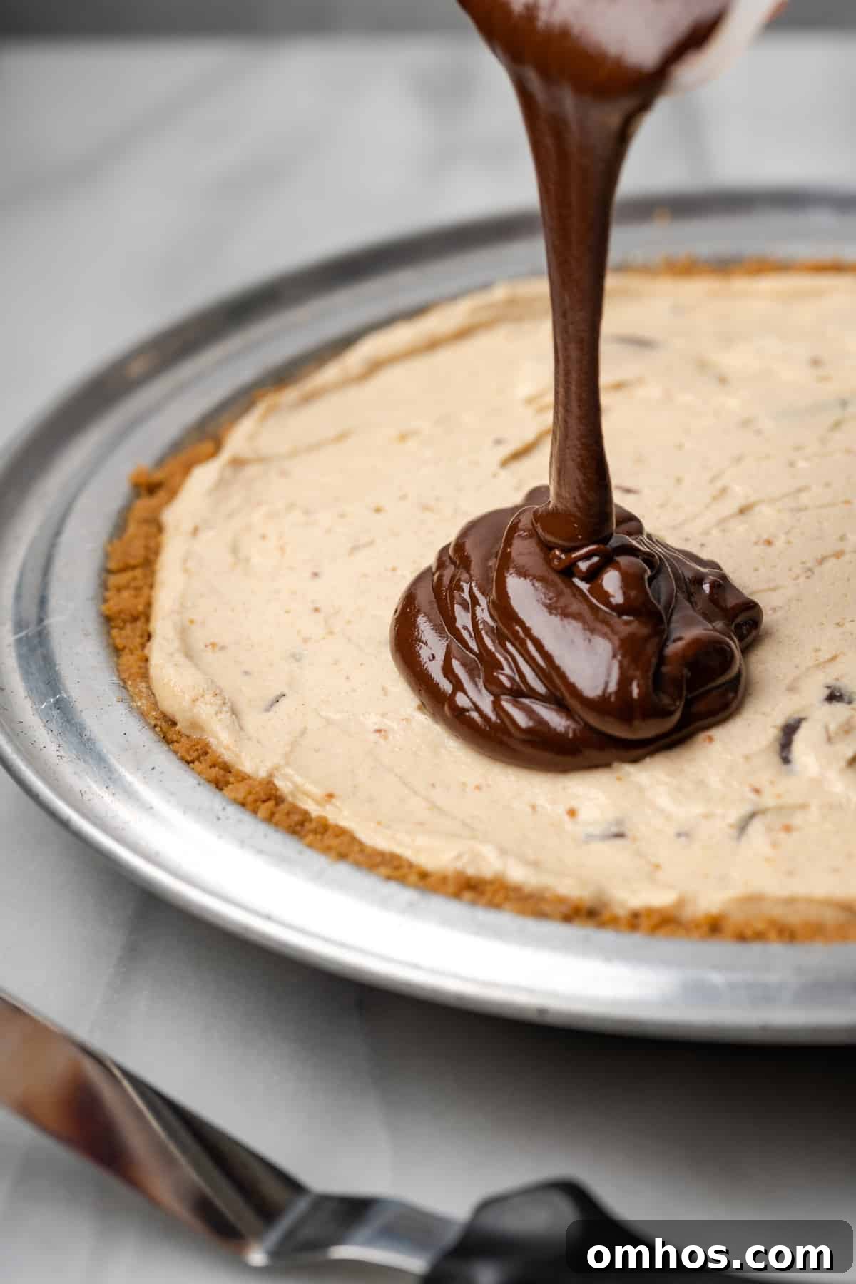 Chocolate ganache being poured on top of a chilled peanut butter pie.