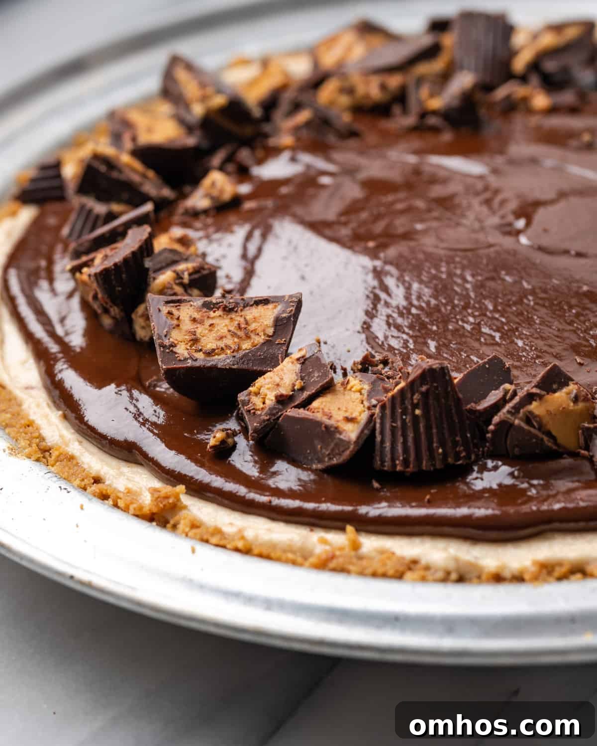 A gluten free peanut butter pie shown with melted chocolate topping and chopped peanut butter cups.