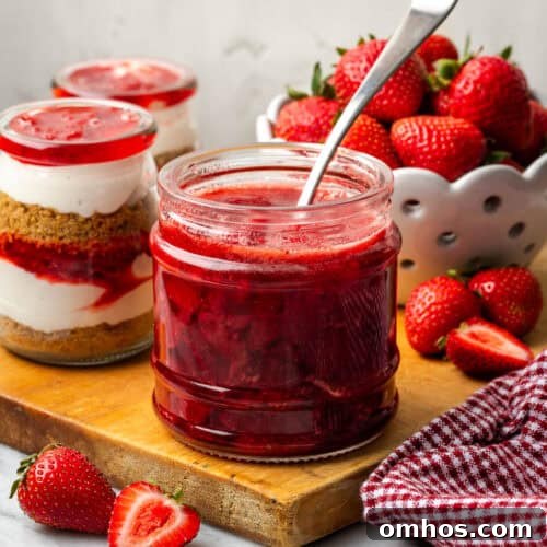 A jar of strawberry compote sitting next to a bowl of fresh berries.