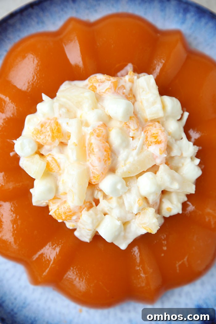A bundt shaped orange sherbet jello salad filled with ambrosia salad in the center on a large round, blue plate.
