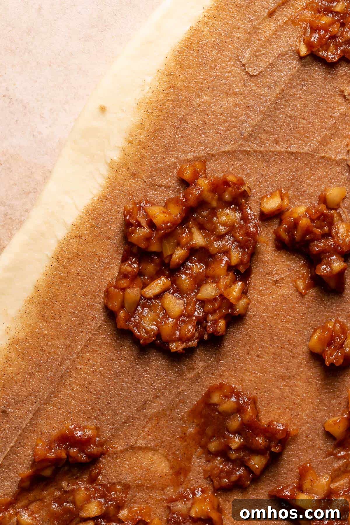Apple filling being spread across the cinnamon sugar filling on the cinnamon roll dough.