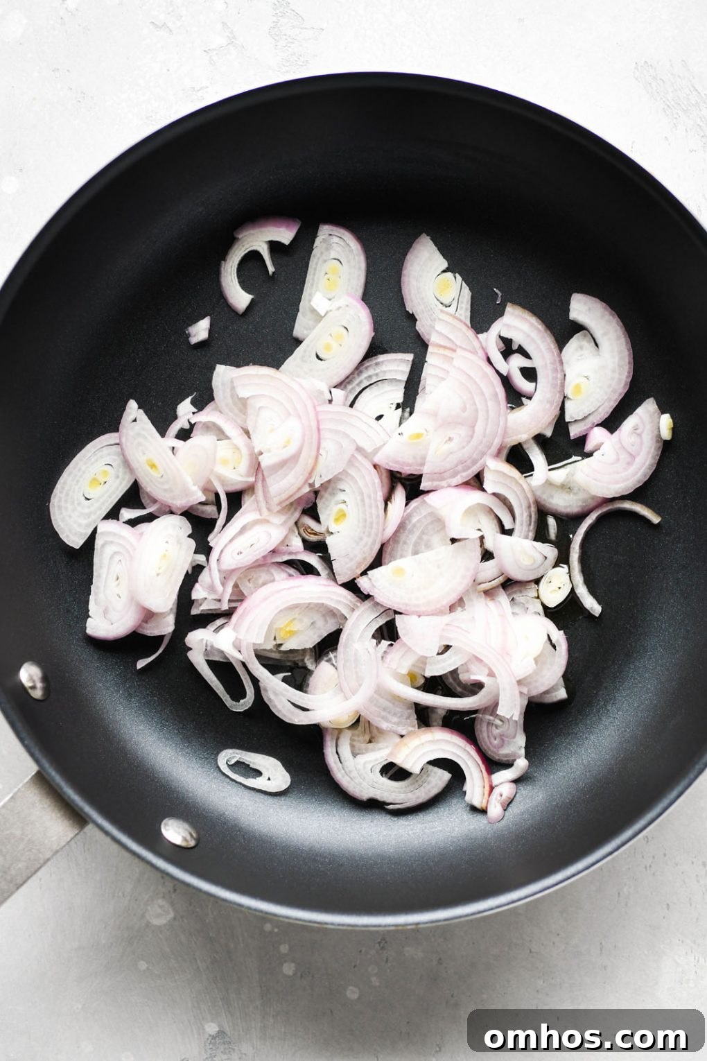 Overhead shot of a medium sized non stick skillet filled with raw thinly sliced shallots.