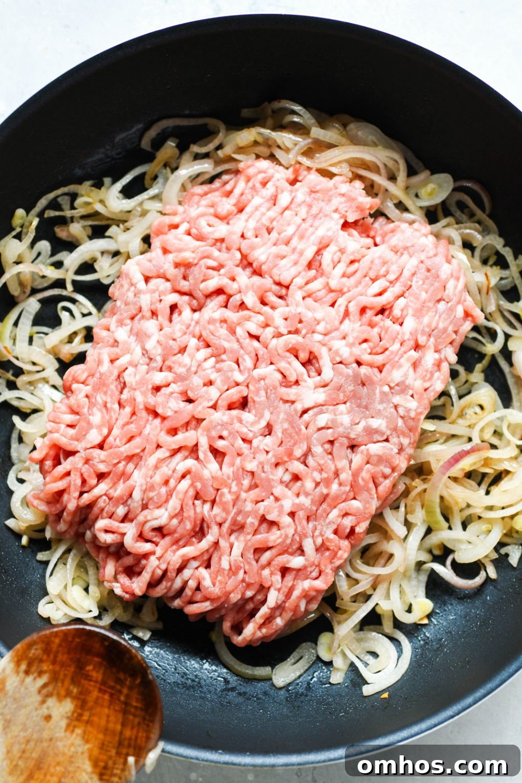 Overhead shot of a medium sized non stick skillet filled with caramelized thinly sliced shallots and raw ground pork.