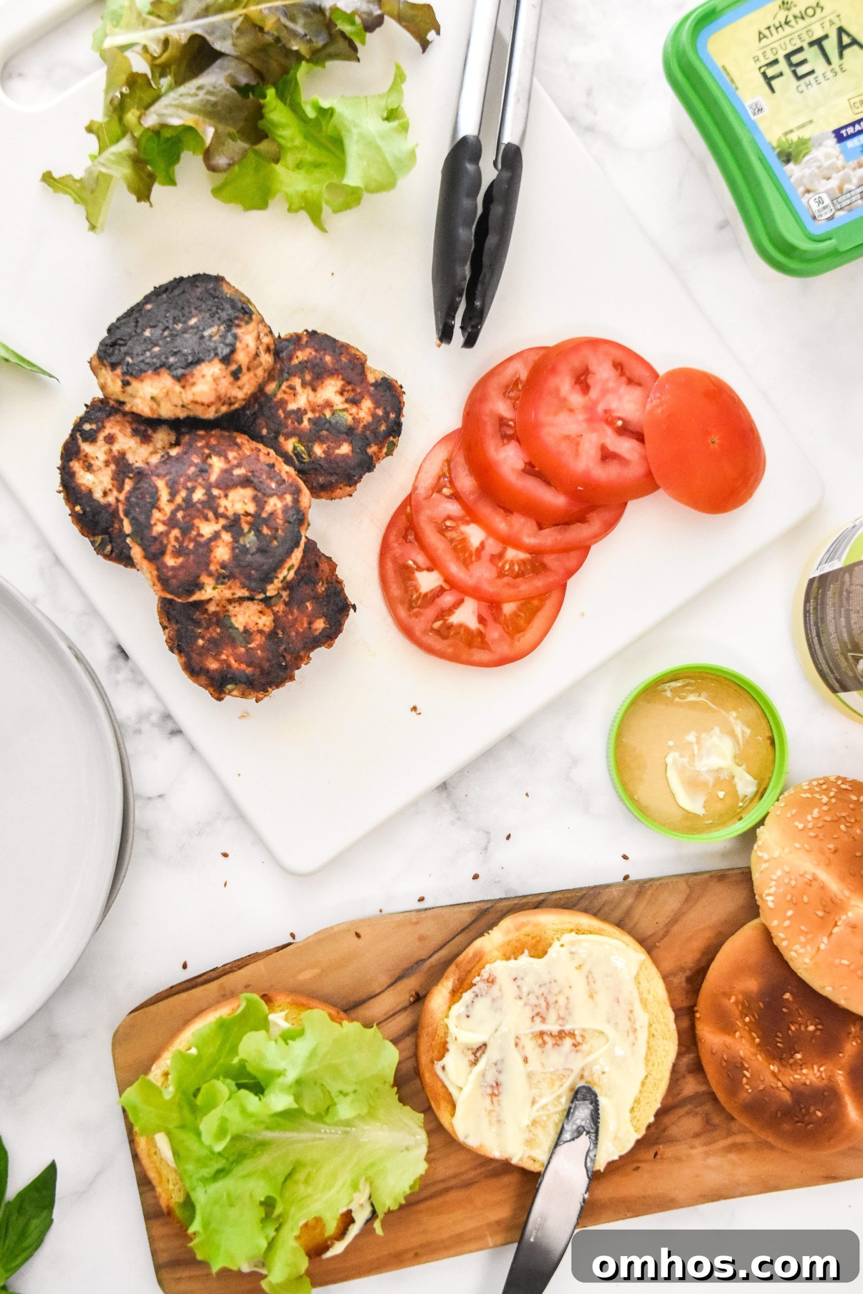 burger toppings, cooked burgers and buns on cutting boards.