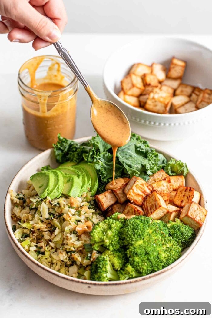 Drizzling sauce over a bowl with tofu, vegetables and avocado.