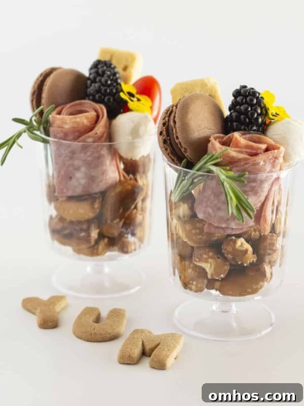Two individual charcuterie cups filled with food and served in a clear glass.