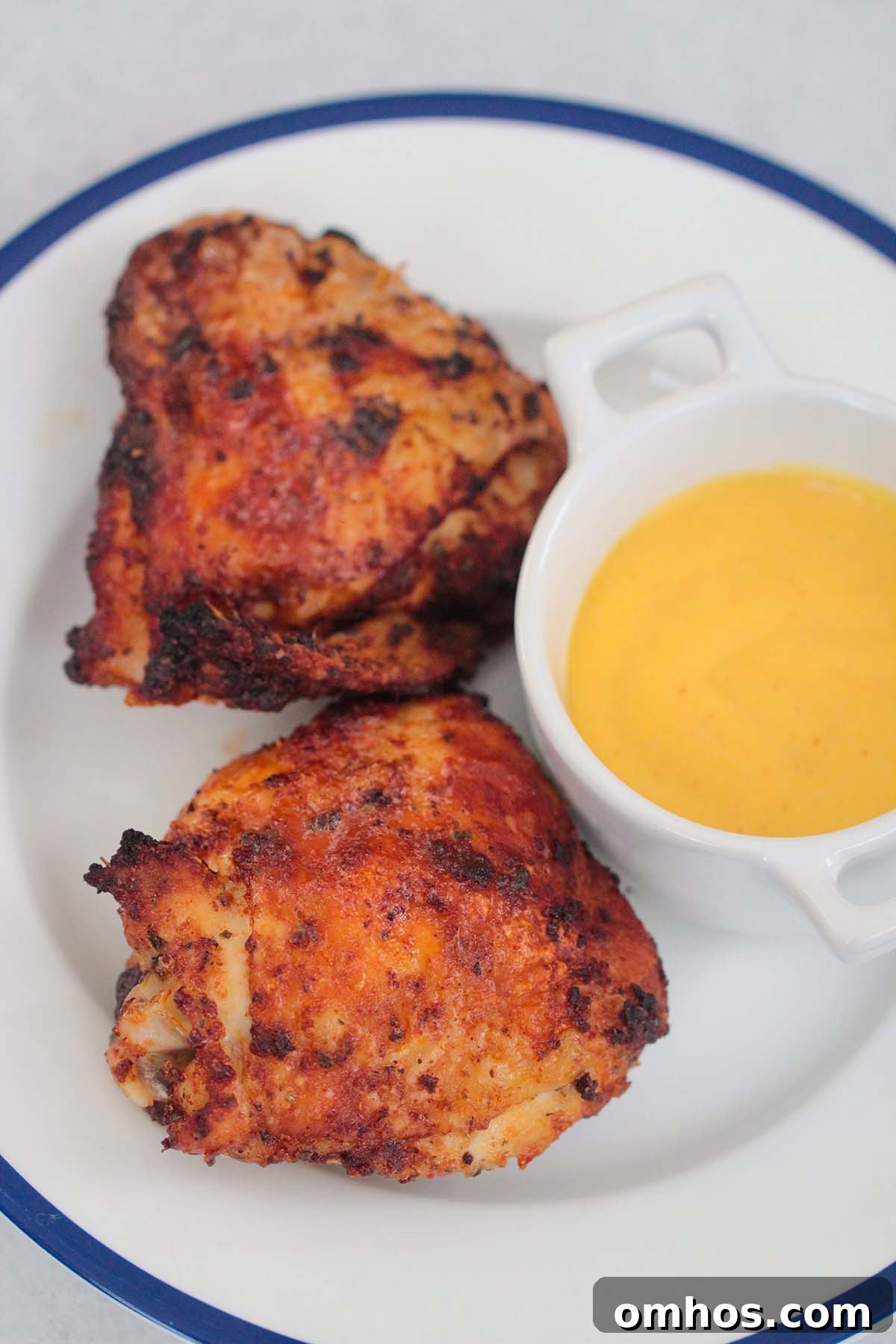 two air fryer chicken thighs on a plate with a side of honey mustard