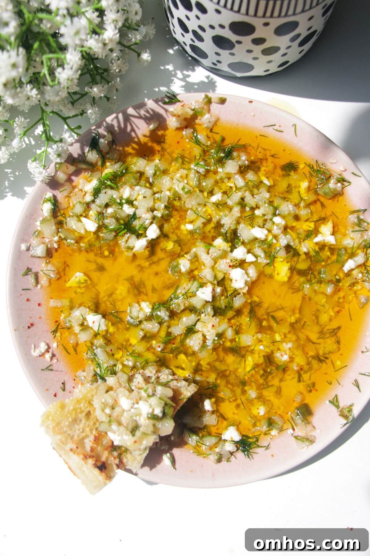 Dill pickle dipping oil on a pink plate with a piece of focaccia on the side.