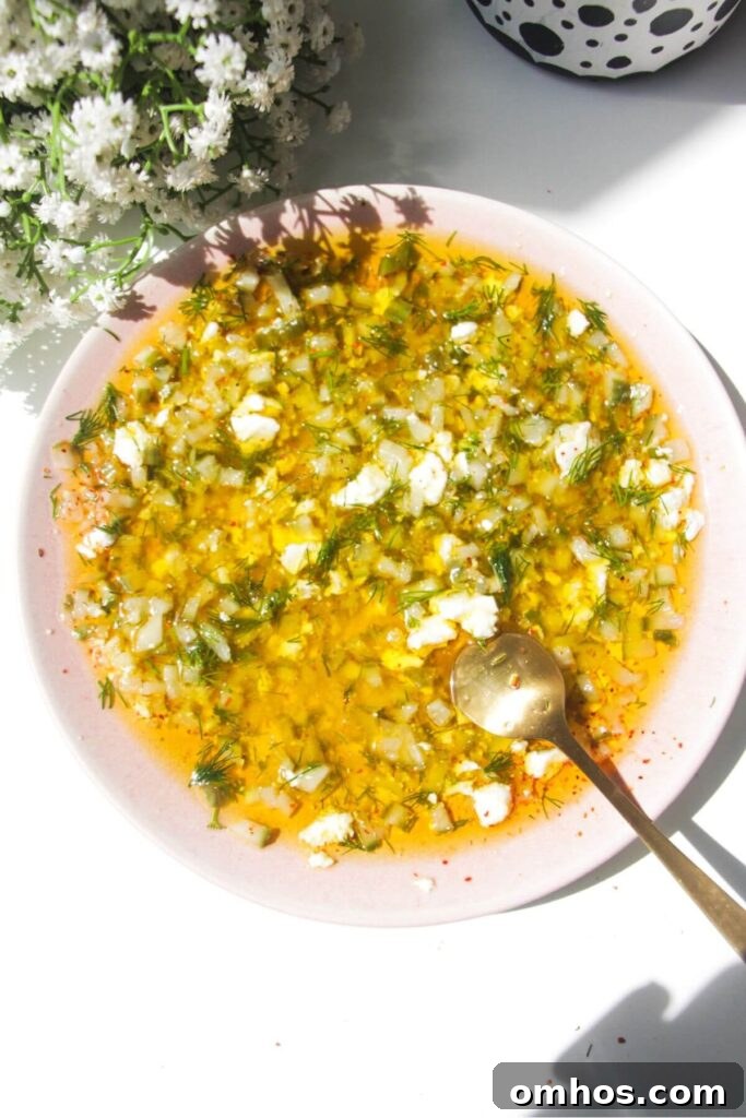 Dill pickle dipping oil mixed in a small pink plate with a gold spoon on the side.