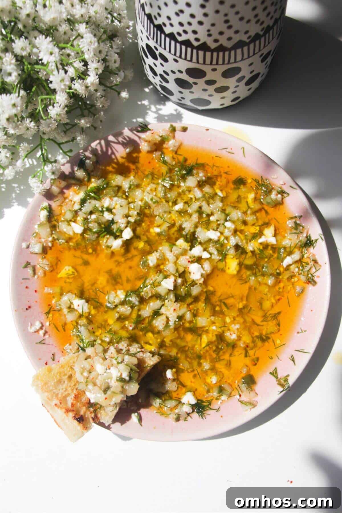 Dill pickle dipping oil on a pink plate with a piece of focaccia on the side.