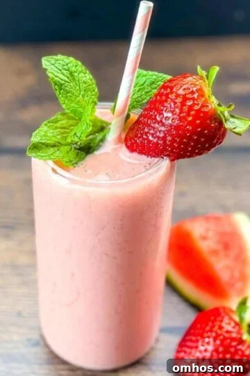 Watermelon smoothie in a tall glass, garnished with fresh mint and strawberry.