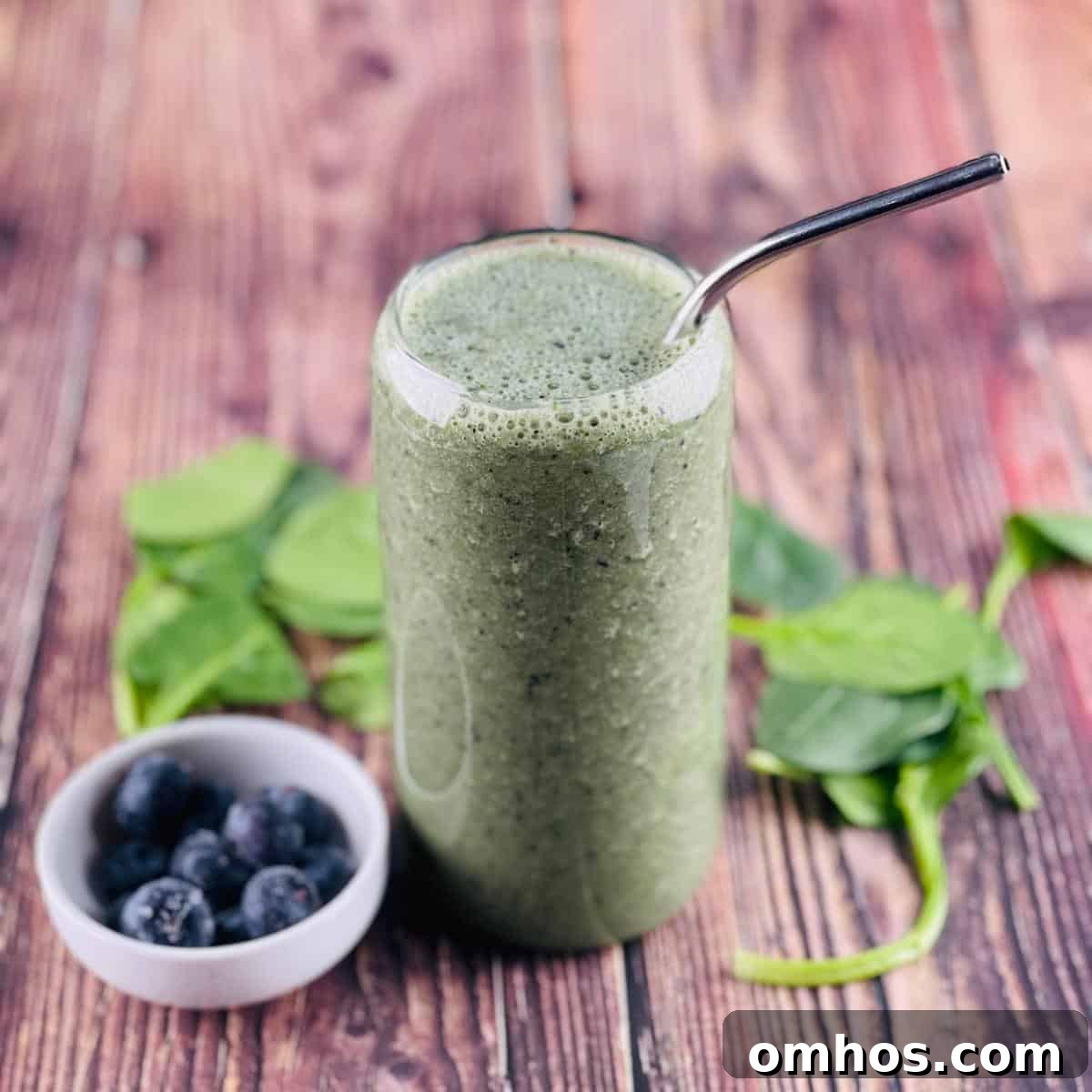 Spinach Banana Smoothie Recipe 5 The spinach smoothie poured into a tall glass, with blueberries and spinach leaves beside the glass.