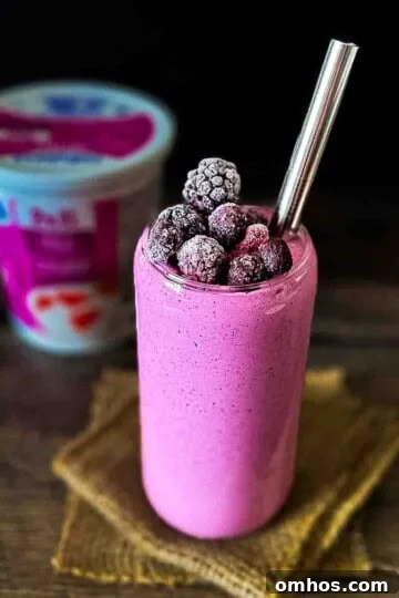 A glass filled with a purple berry smoothie with cottage cheese, with a container of cottage cheese in the background.