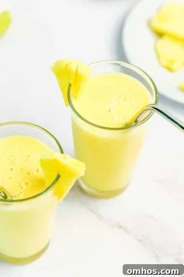 A closeup of a mango pineapple smoothie in 2 glasses with straws.