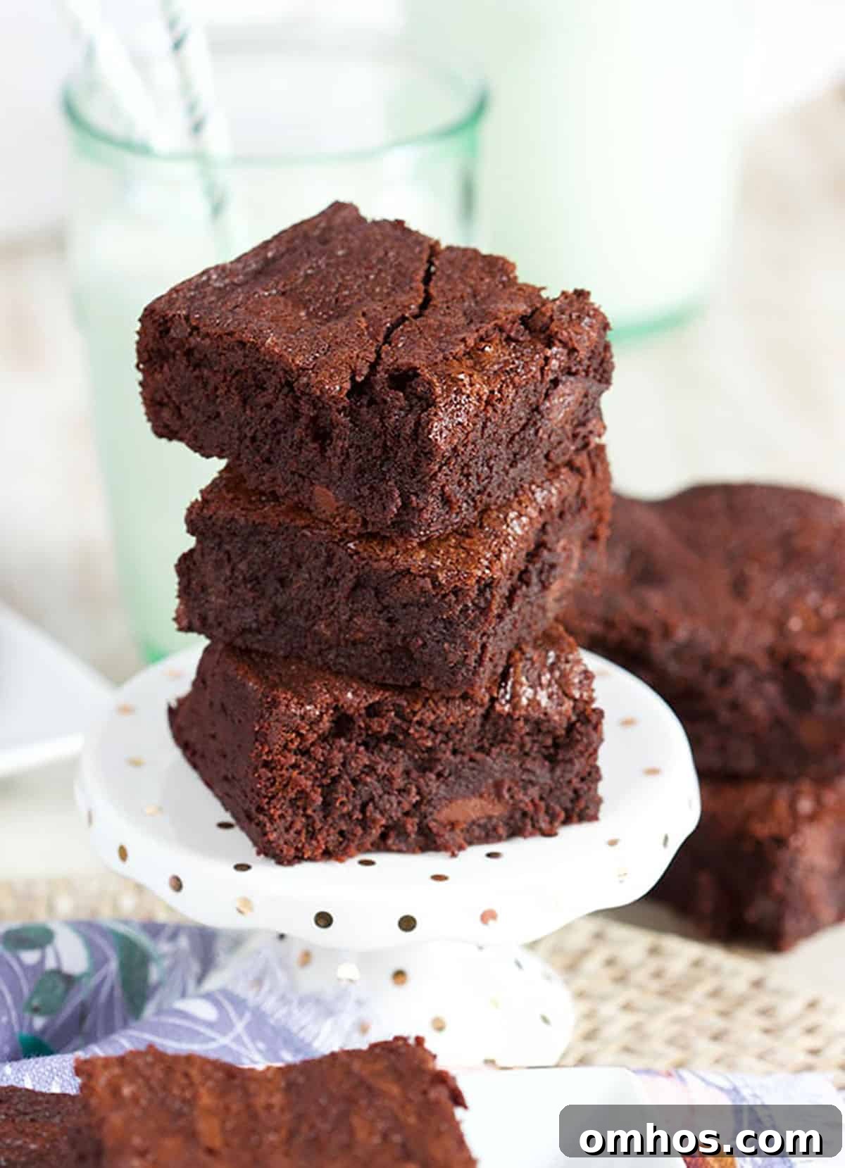 Three brownies stacked on a mini cake plate with a glass of milk in the background.