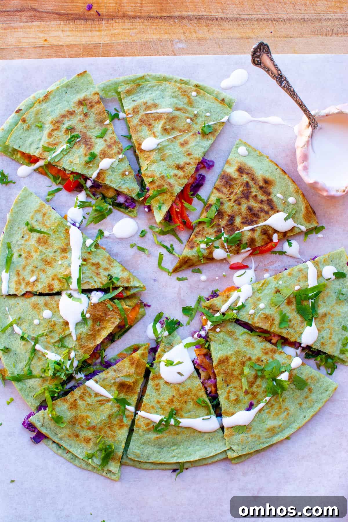 How to Make a Rainbow Vegetable Quesadilla 7 Overhead image of a veggie quesadilla on a cutting board with a pink little bowl of sour cream on the side.