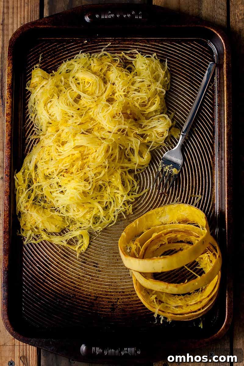 Spaghetti Squash Marinara with Chili Oil Tomato Garlic Bread 3 Vertical image of the cooked interior of spaghetti squash and its skin and a fork on a sheet pan.
