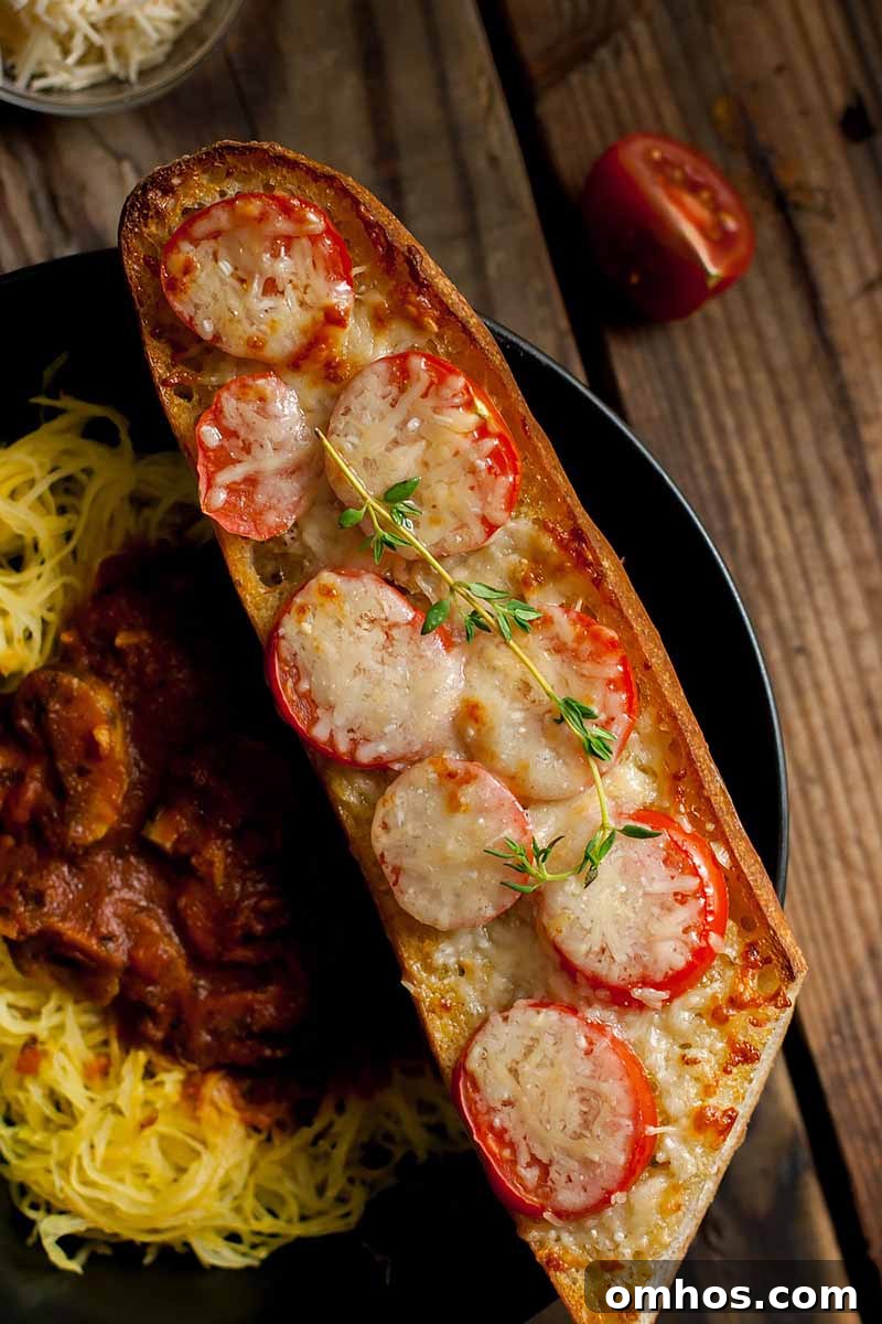 Spaghetti Squash Marinara with Chili Oil Tomato Garlic Bread 8 Vertical image of bread topped with sliced small tomatoes, melted cheese, and herbs on a wooden surface.
