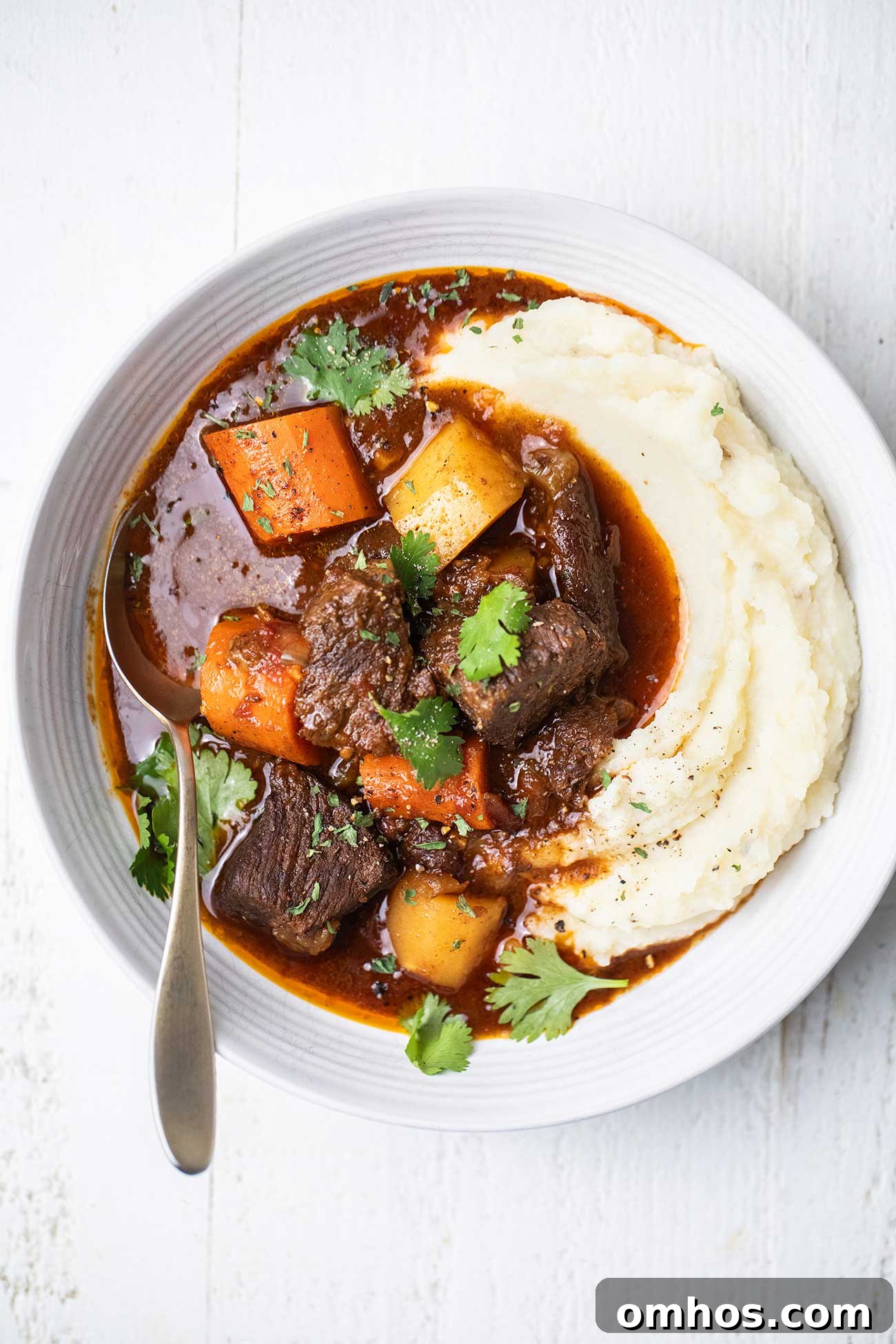 Moroccan Beef Tagine Recipe: Spiced Slow-Cooked Stew 2 A bowl of Moroccan Beef Stew served over a bed of mashed potatoes in a white bowl.