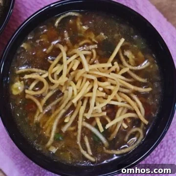 chicken Manchow soup in a black bowl with crispy fried noodles on the top.