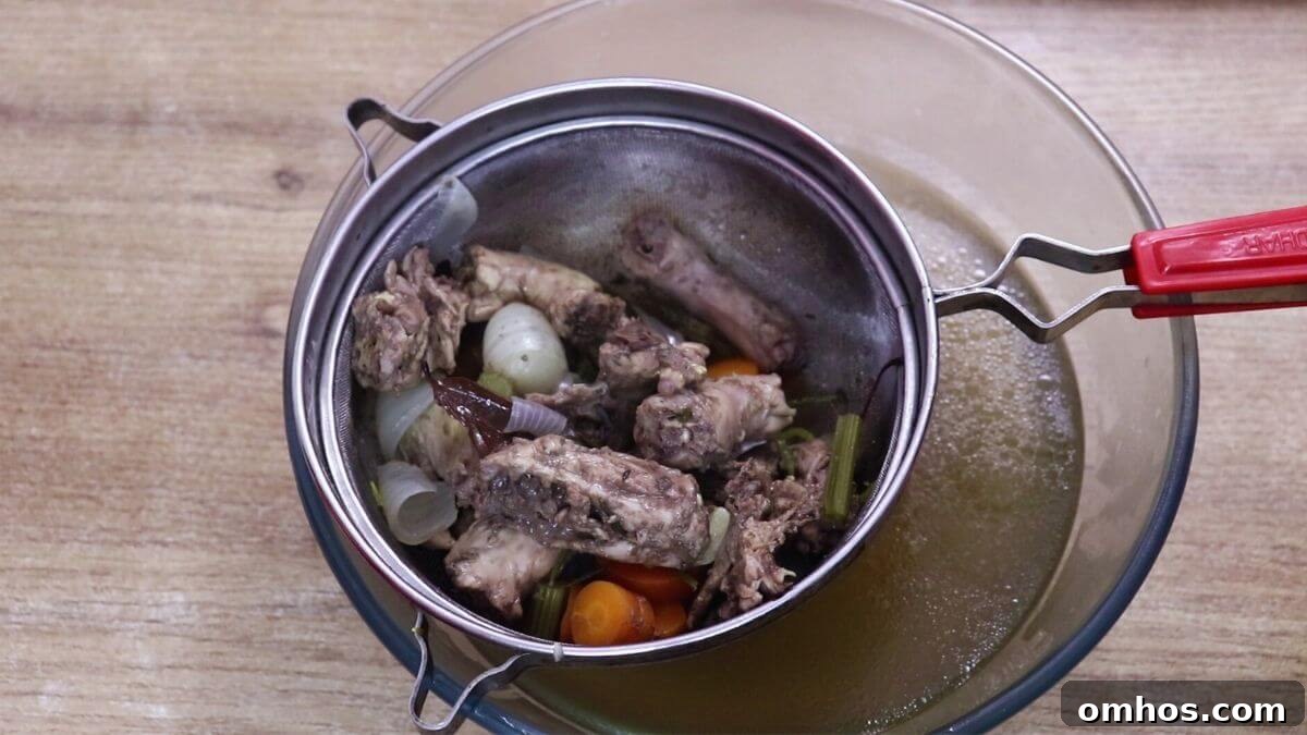 Homemade chicken stock being strained through a fine mesh sieve.
