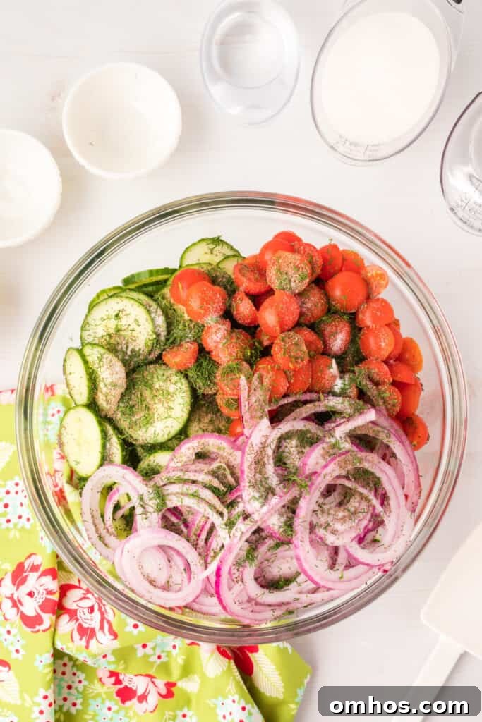 Salad ingredients in a glass bowl topped with fresh dill, salt, and celery seed