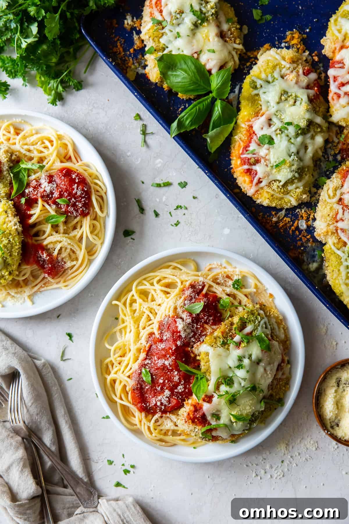 An over the top shot of chicken pesto parmesan with pasta on white plates.