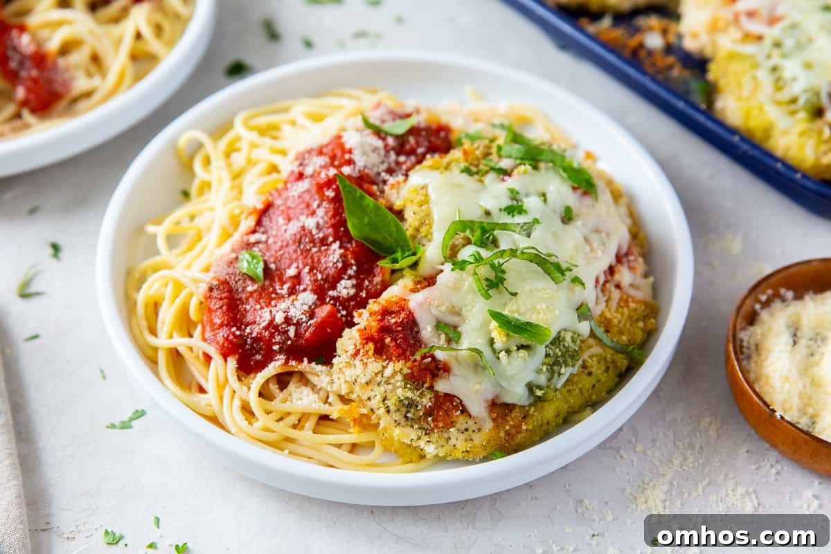 Pesto Chicken Parmesan on pasta in a white dish.