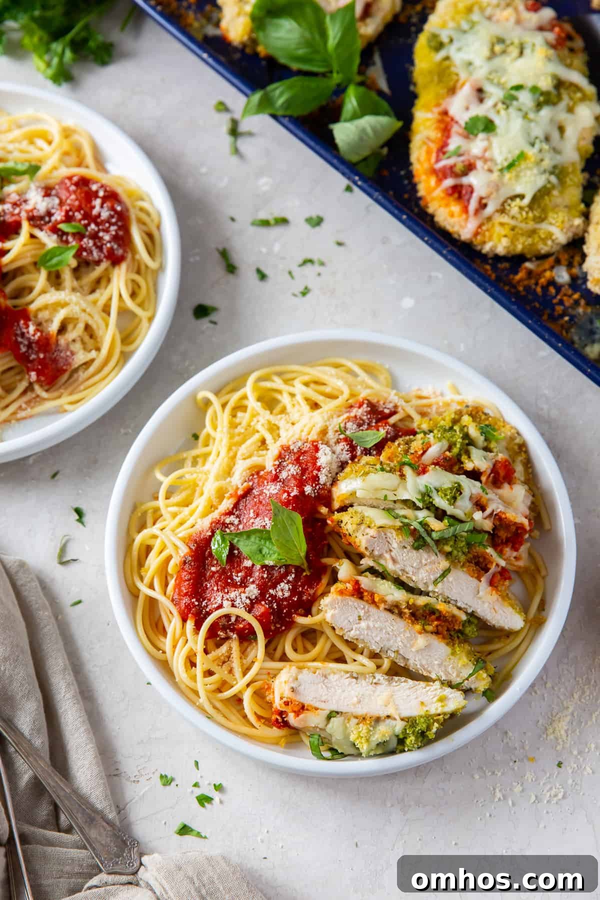Sliced Chicken Pesto Parmesan in a white dish with pasta and marinara sauce.