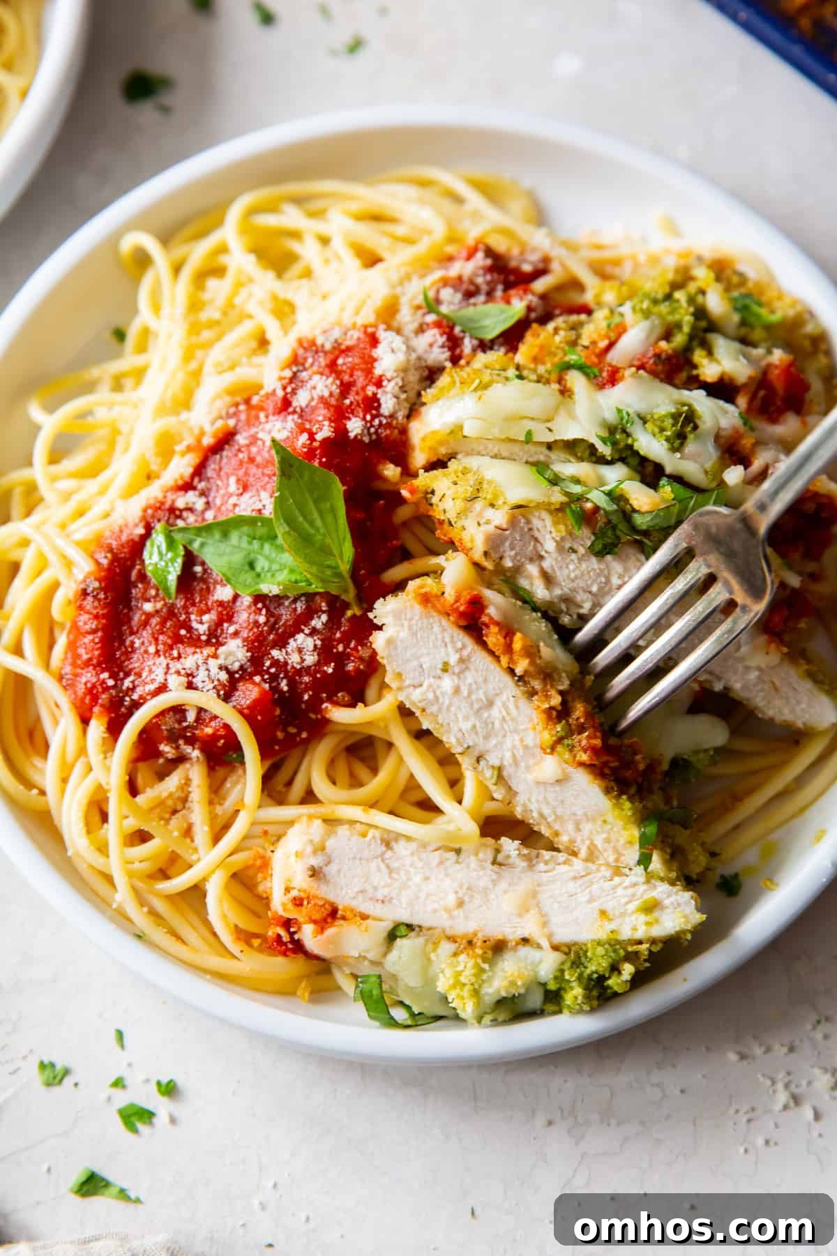 A fork pierces a slice of Chicken Pesto Parmesan.