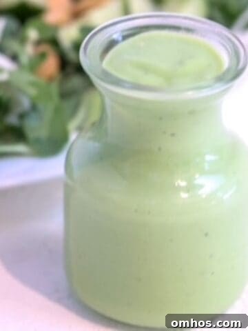 Green goddess dressing in a glass carafe in front of a green salad.