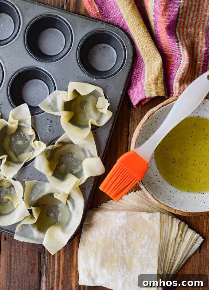 Wontons in mini muffin tin with olive oil and brush. A pink napkin sits next to them.
