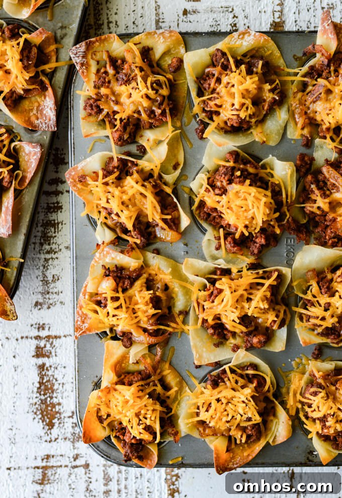 A mini muffin tin is filled with cooked taco wontons and shredded cheese sprinkled on top.