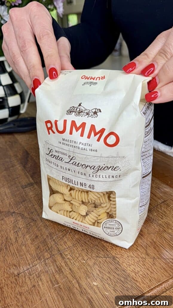 A person with red nail polish holds a white bag of Rummo Fusilli No. 48 pasta on a wooden surface.