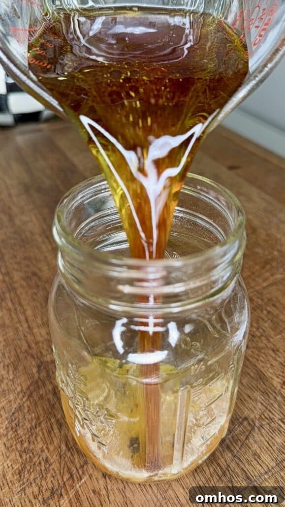 Amber-colored dressing being poured from a glass measuring cup into a mason jar.