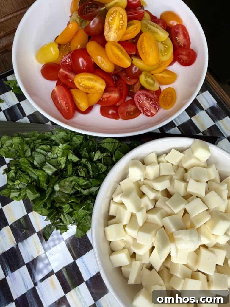 A bowl with halved cherry tomatoes, cubed mozzarella, and chopped basil on a checkered cloth.