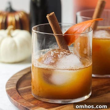 Fall pumpkin bourbon cocktail on table with ice cube and cinnamon stick.