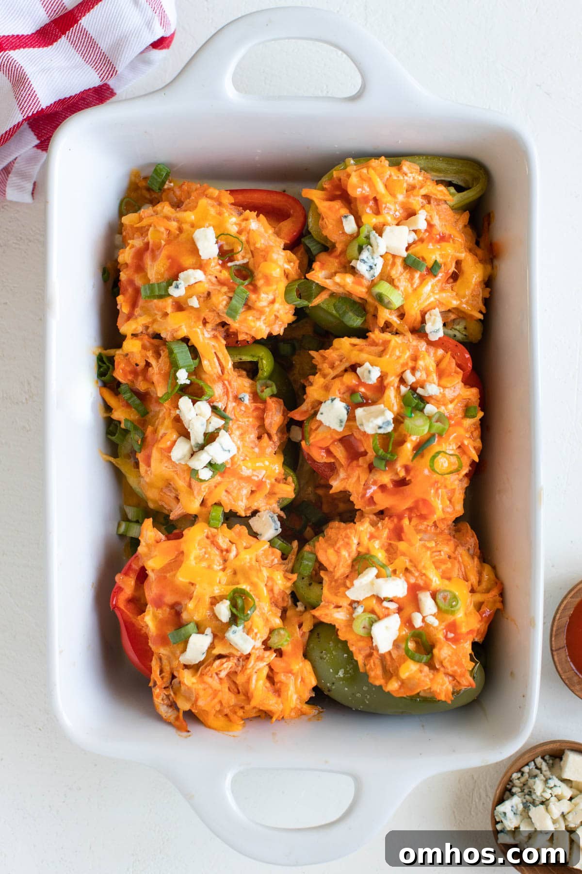 chicken stuffed bell peppers in a white casserole dish topped with bleu cheese and green onions
