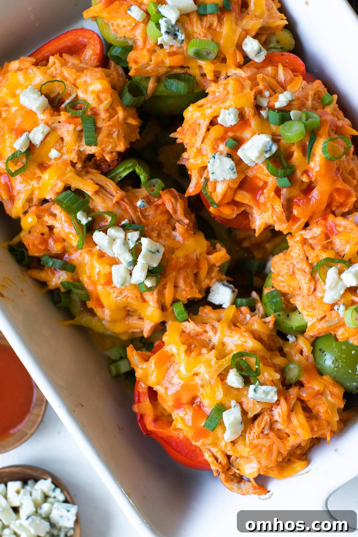chicken stuffed bell peppers in a white casserole dish topped with bleu cheese and green onions