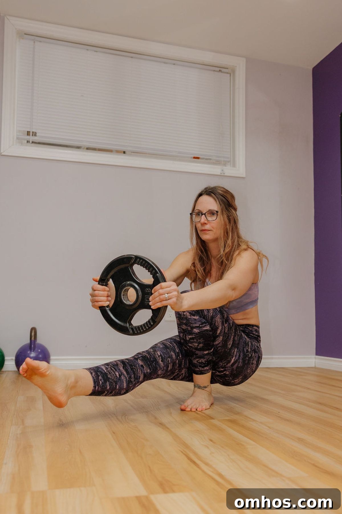 How to Make Home Workouts More Intense Without Weights 4 Woman in a single leg squat holding a weight plate.