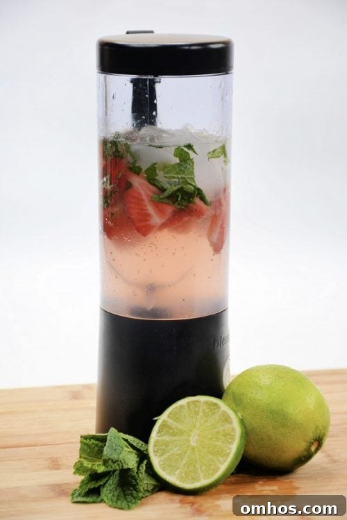 How to Make a Fresh Strawberry Mojito 2 strawberries, rum, mint, and ice in a clear blender with a black top.