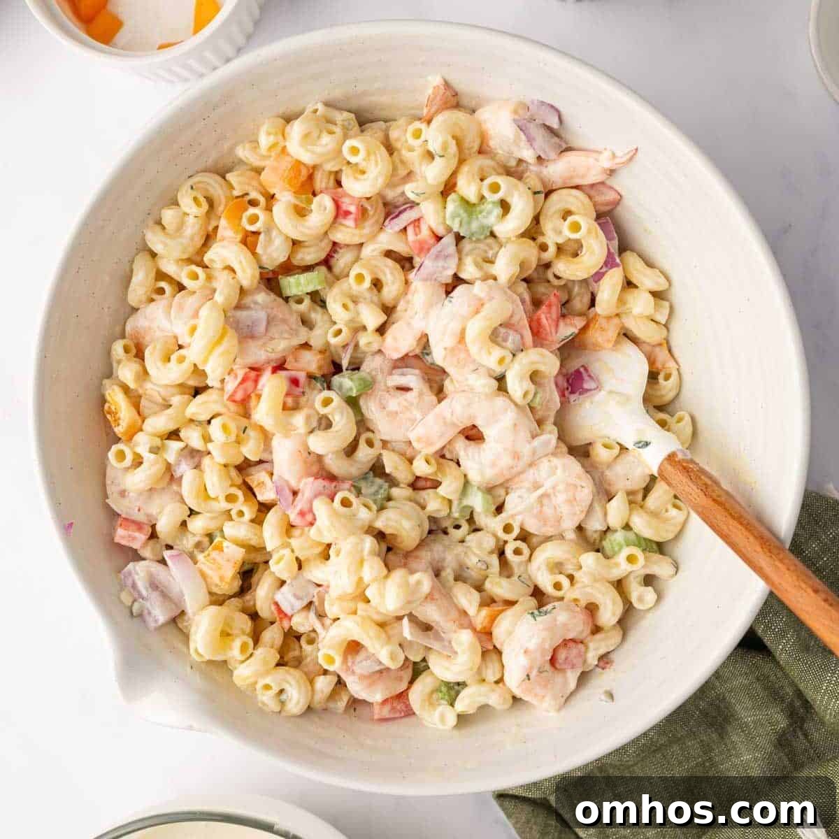 A spatula is used to combine macaroni, shrimp and salad dressing.