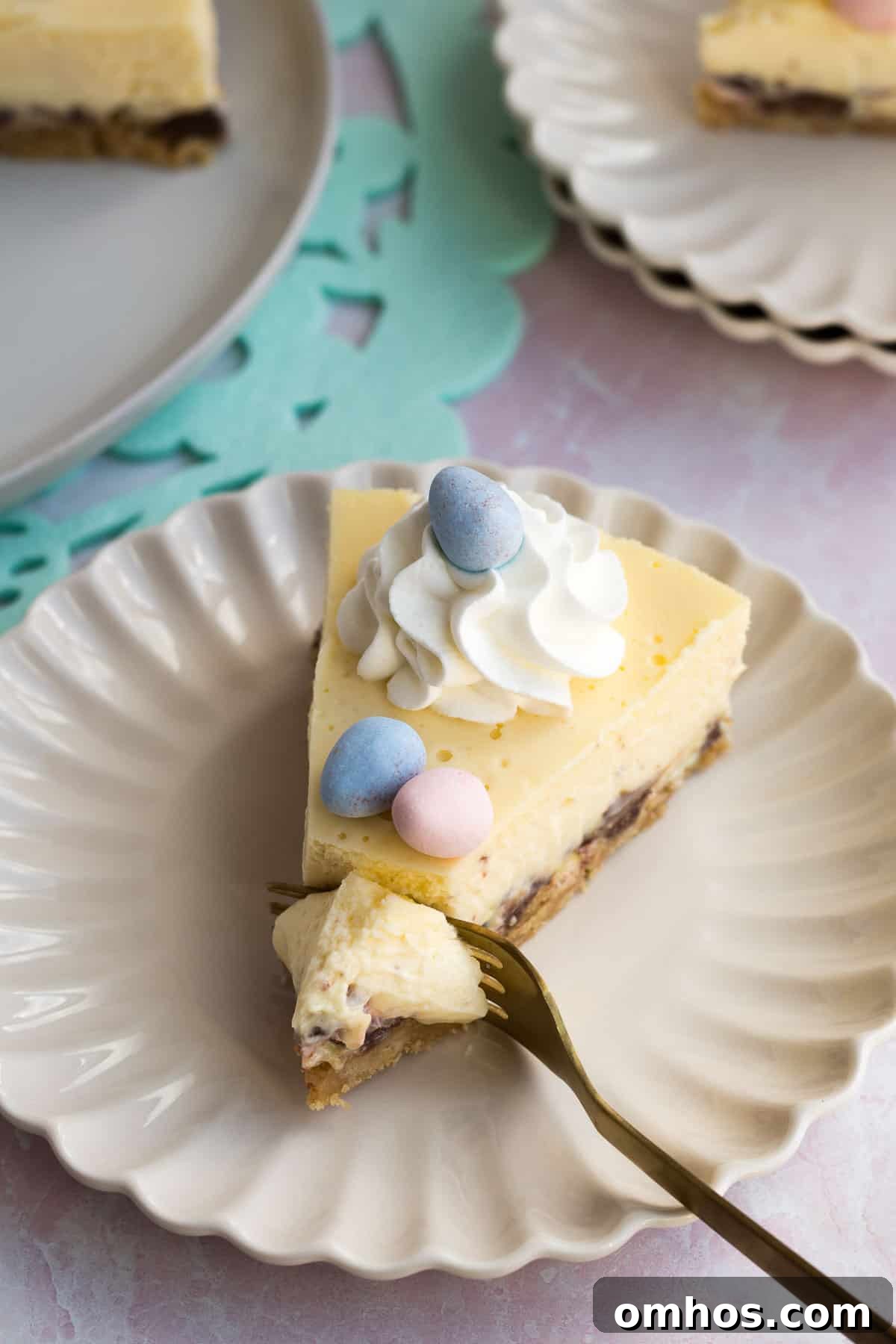 No-Bake Easter Egg Cheesecake Recipe 3 a cream scalloped plate with a slice of easter egg cheesecake with a gold fork cutting into it