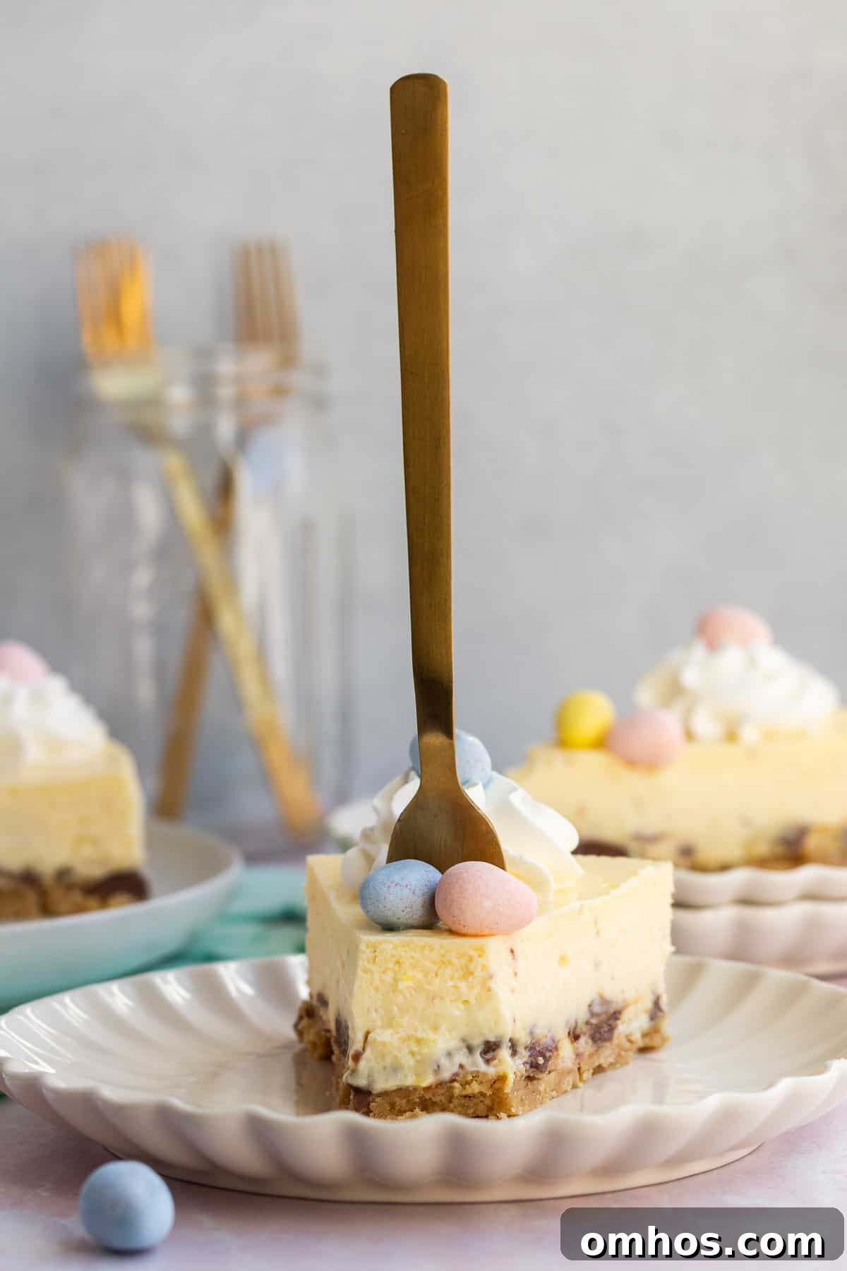 No-Bake Easter Egg Cheesecake Recipe 5 a slice of Easter egg cheesecake on a plate with a gold fork sticking up straight in it and other slices in the background